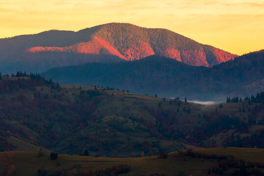 transcarpathian rural landscape at sunrise. countryside scenery of carpathian mountains in autumn. trees and fields on rolling hills. clouds and mist glowing in the morning light
