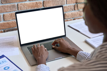 Young black African business woman using laptop computer device white blank empty mockup template screen digital technology working online, typing sitting at desk at home office. Over shoulder view