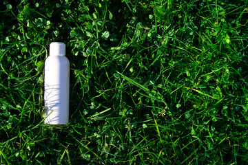 in the green grass lies a white bottle with cosmetics. autumn aroma of morning frosty freshness.