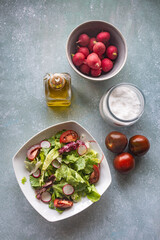 Plato de ensalada visto desde arriba, con lechuga, tomate, rábanos, sal y aceite de oliva