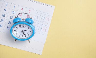 Alarm clock with calendar on yellow background.