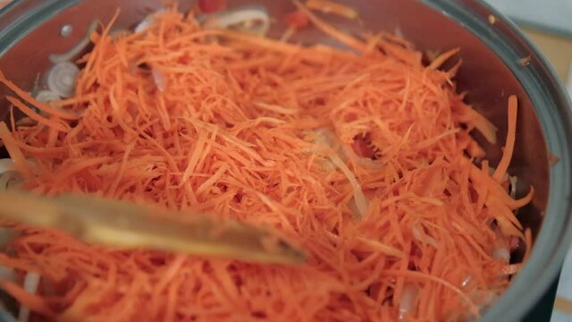 Wooden spoon stirring yam, carrots, tomato, and onion slices in pot