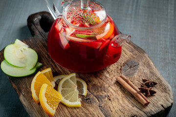 Red fruit tea in a teapot with berries and citrus fruits. Autumn tea with natural fruits on wooden board