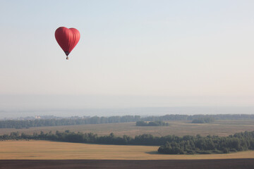 A beautiful red balloon in the shape of a heart on the background of an autumn field. The concept of love and Valentine's Day. a romantic date together. a declaration of love in the sky.