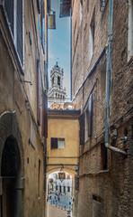 Narrow alley in Siena under a blue sky with clouds