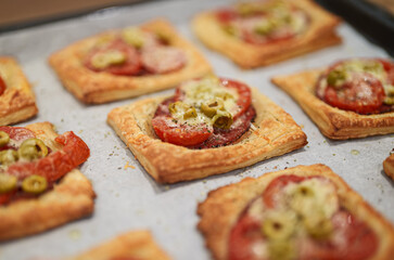 Baked square mini pizzas with salami, cheese, olives and tomato.