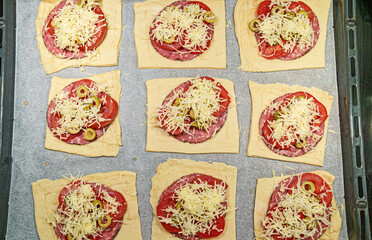 Square mini pizzas with salami, cheese, olives and tomato.