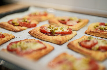 Baked square mini pizzas with salami, cheese, olives and tomato.
