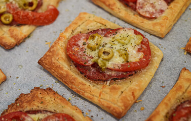 Baked square mini pizzas with salami, cheese, olives and tomato.