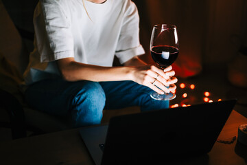 Young millennial woman having video call on laptop computer and drinking wine, use technology for communicate with friends or family.