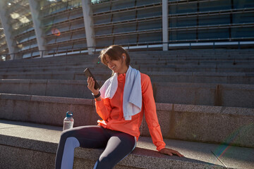 Smiling sportswoman train outdoors using modern smartphone