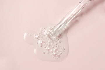 Liquid oil serum drop in pipette isolated on pastel pink background. Retinol, aha, bha acid, collagen skincare fluid, photo with shallow depth of field. Gold essence in dropper for beauty treatment