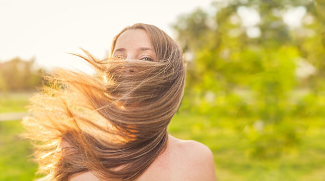 Happy lady face wrapped in her long blond hair by blow of the wind, joyness and freedome outside, warm summertime image