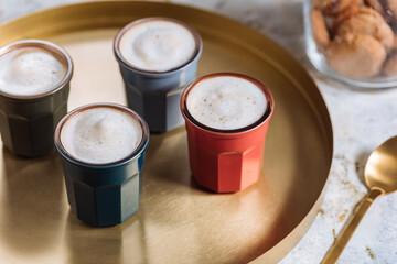 Macchiato in four different cups on a golden tray with golden spoon and cookies in jar 