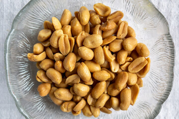 Close up of salted peanuts in a glass bowl. Overhead view with white background