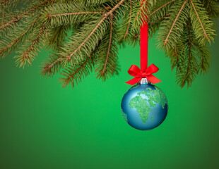 Globe christmas ornament hanging from a tree branch on green with a red bow. Peace on Earth, eco friendly or winter travel concept.