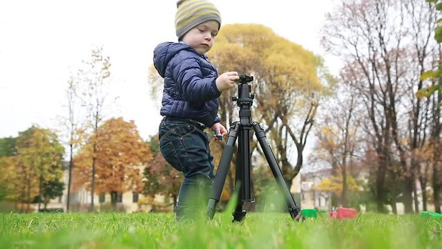A kid on a walk in the park, a child with interest examines a professional tripod operator