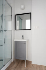 Bathroom with modern shower and bathtube with glass. Cabinet with sink and mirror on the white wall. Minimalism in interior. Vertical.