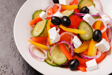 greek salad with tomatoes, cucumbers, olives, pepper and soft feta cheese in a  plate on a dark