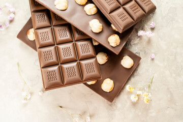 Milk chocolate bar with whole hazelnut kernels, flowers on white background. Healthy food concept, delicious chocolate sweets for kids, diet, sugar