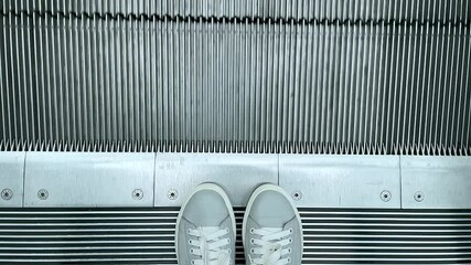Feet in grey sneakers standing near escalator steps in the shopping mall
