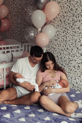 Loving family with newborn twins. Twins sleeping in mother's and father's arms. Baloons for birthday. Selective focus. Film grain