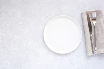 White plate with silver cutlery on grey