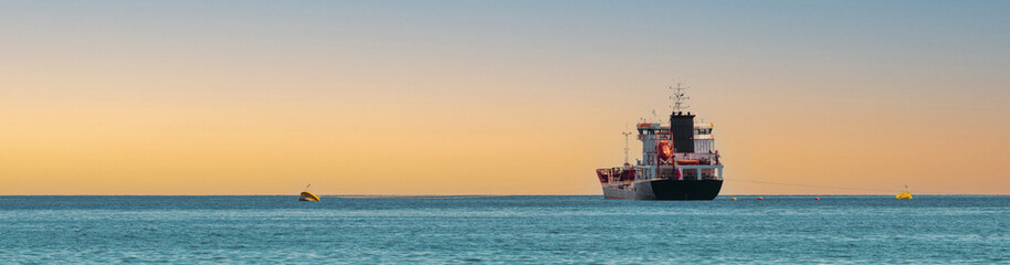 Panoramic shot of transport ship traveling on open sea at sunset.