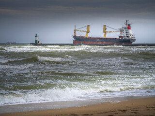 trade ship behind pier and lighthouse at storm sea