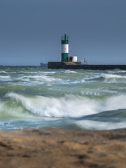 view from beach to lighthouse in storm sea under blue sky