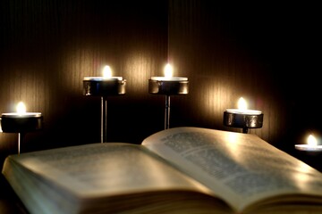 An open book in the light of burning candles. A dark and cozy atmosphere in the library. Reading,...