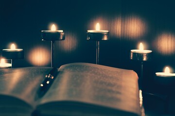 An open book in the light of burning candles. A dark and cozy atmosphere in the library. Reading,...