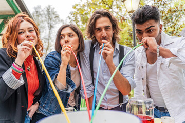 group of multi-cultural friends having fun at the garden party sucking beer from colorful straws