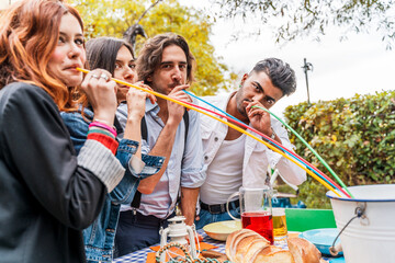 group of multi-cultural friends having fun at the garden party sucking beer from colorful straws