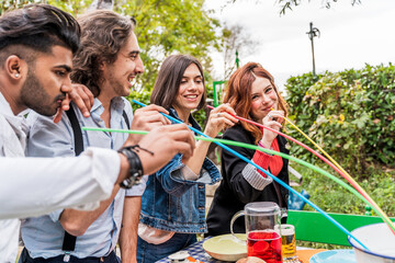 group of multi-cultural friends having fun at the garden party sucking beer from colorful straws