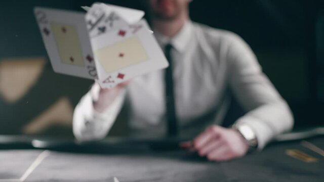 A professional croupier is working with cards. Close up of holdem dealer with playing cards on black table. Concept of casino gambling or poker and entertainment. Slow motion