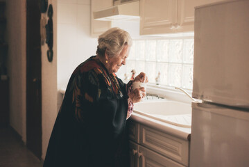 Smiling senior woman in warm clothes with mug near sink
