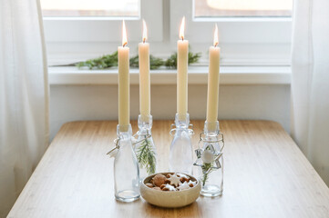 Four candles in bottles is lit for Advent, Christmas cookies and decoration on a table near the...