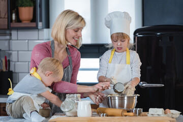 Mother with son and daughter having fun in the kitchen playing with dough, baking