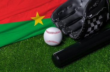 Baseball bat, glove and ball near Burkina Faso flag on green grass background