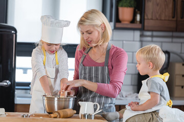 Mother with son and daughter having fun in the kitchen playing with dough, baking