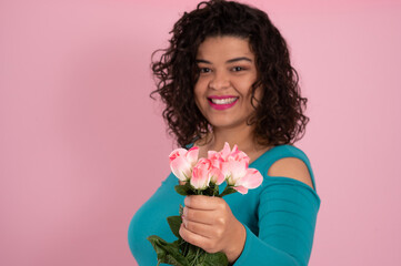 young woman smiling, offering pink flowers on pink background.
