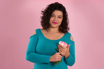 young woman holding bouquet of flowers near to her chest and looking at camera on pink background.