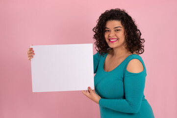young latin woman holding a white blank board, looking at camera on pink background