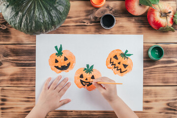 Step-by-step Halloween tutorial pumpkin apple prints. Step 10: Child hand draws eyes, mouth of pumpkins with black paint
