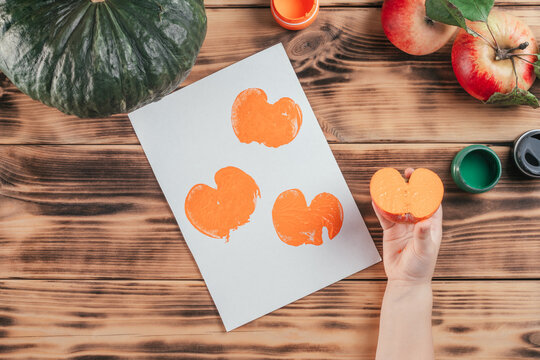 Step-by-step Halloween tutorial pumpkin apple prints. Step 10: Child hand holds half of apple painted in orange gouache