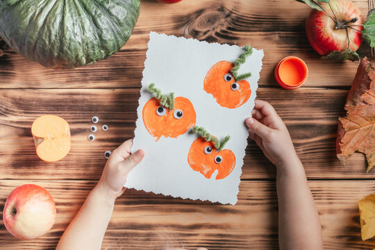 Step-by-step Halloween childrens tutorial pumpkin apple prints. Step 17: Child hands hold finished card, top view