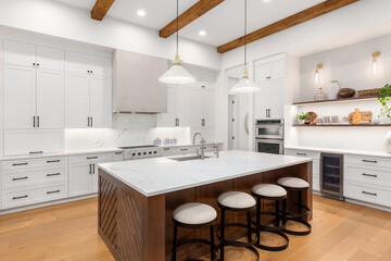 Beautiful white kitchen in new luxury home with large island. Features large island, stainless steel appliances, and sleek modern range hood.
