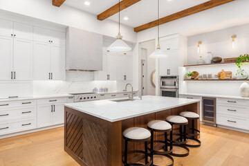 Beautiful white kitchen in new luxury home with large island. Features large island, stainless steel appliances, and sleek modern range hood.