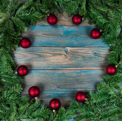 Fototapeta na wymiar Top view of a complete wreath and red ball ornaments in circle border on blue aged wooden planks for the winter holiday season of Christmas or New Year background